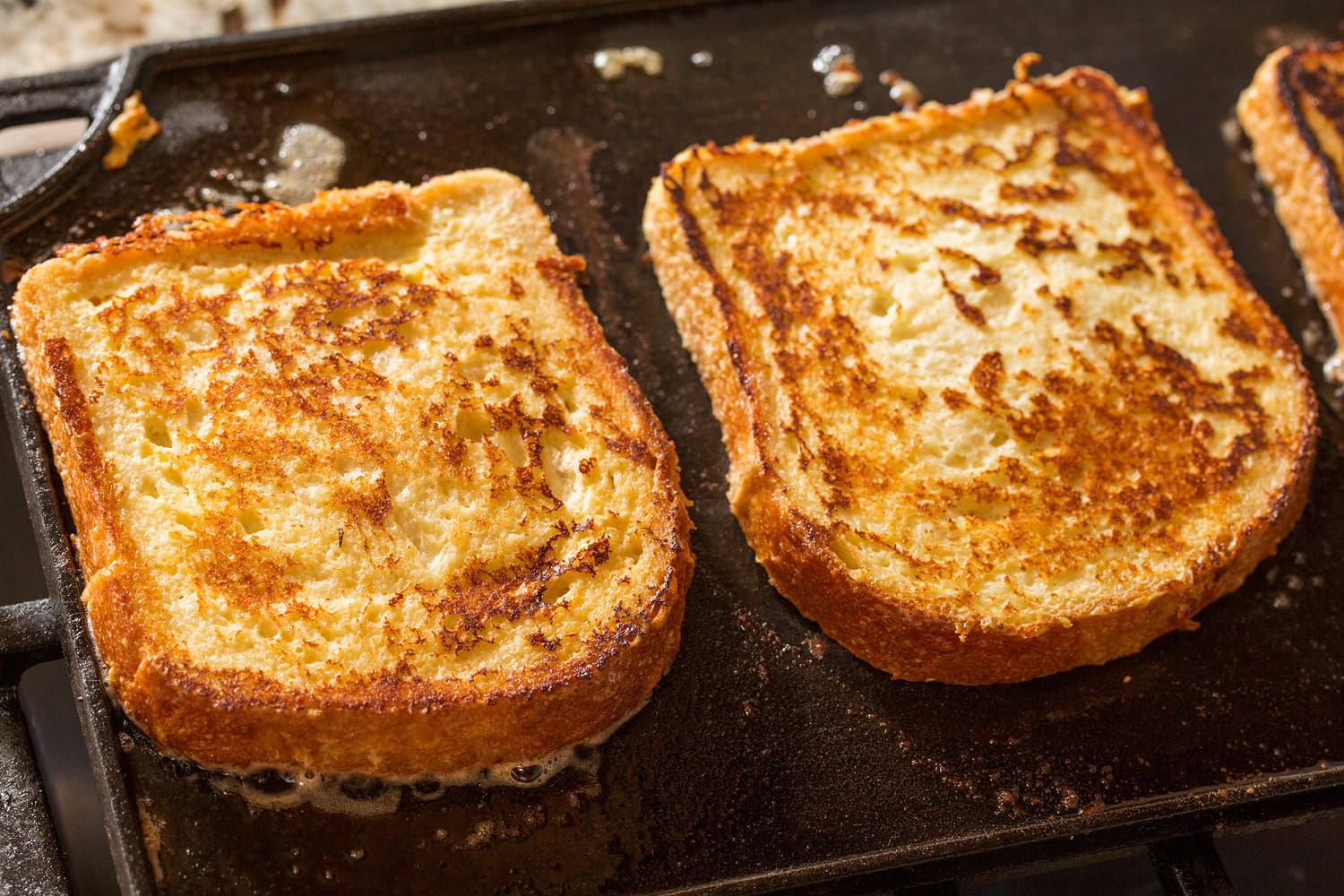 Buttermilk French Toast Slices of french toast cooking on cast iron griddle on second side.