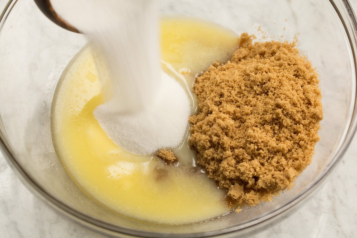 White sugar and brown sugar added to melted butter in glass mixing bowl.