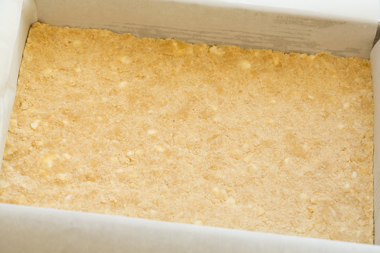 Apple Pie Bars Crust mixture spread in a baking dish with parchment paper.