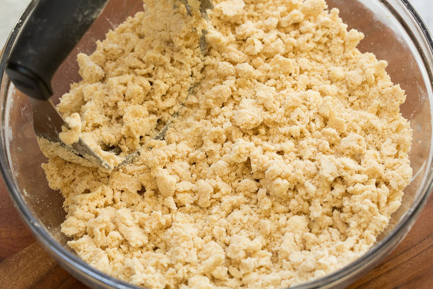 Apple Pie Bars Crumble crust mixture in a glass mixing bowl with a pastry blender.