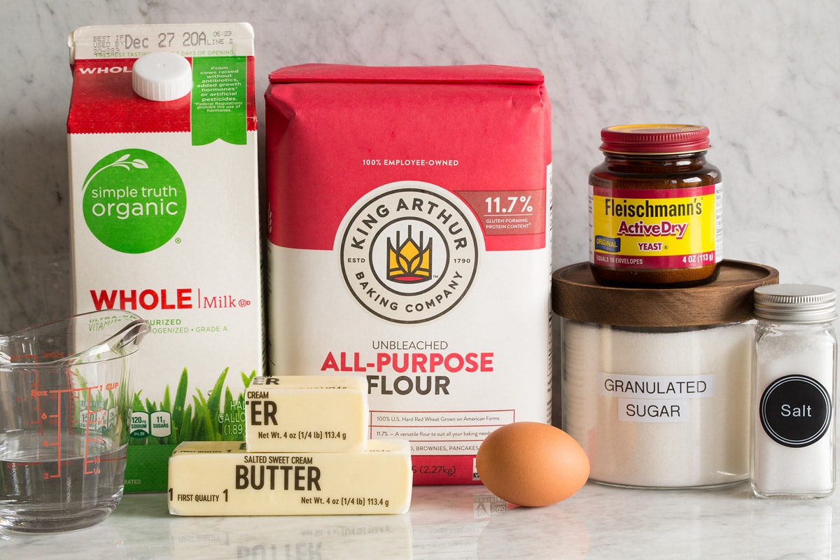 Image of ingredients used to make bread. Includes flour, yeast, butter, egg, milk, salt, sugar and water.