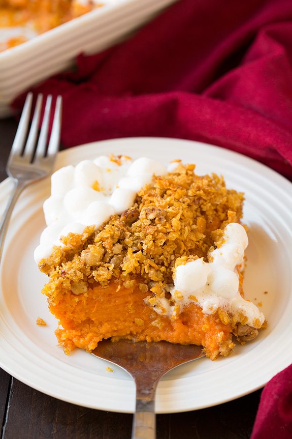 Single serving of sweet potato casserole being scooped onto a white serving plate.