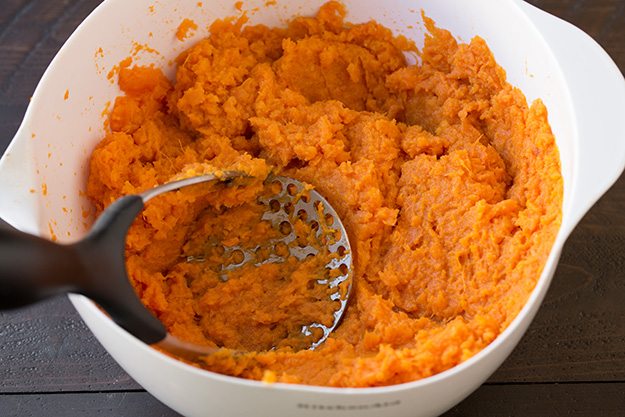 Mashing sweet potatoes in a mixing bowl.