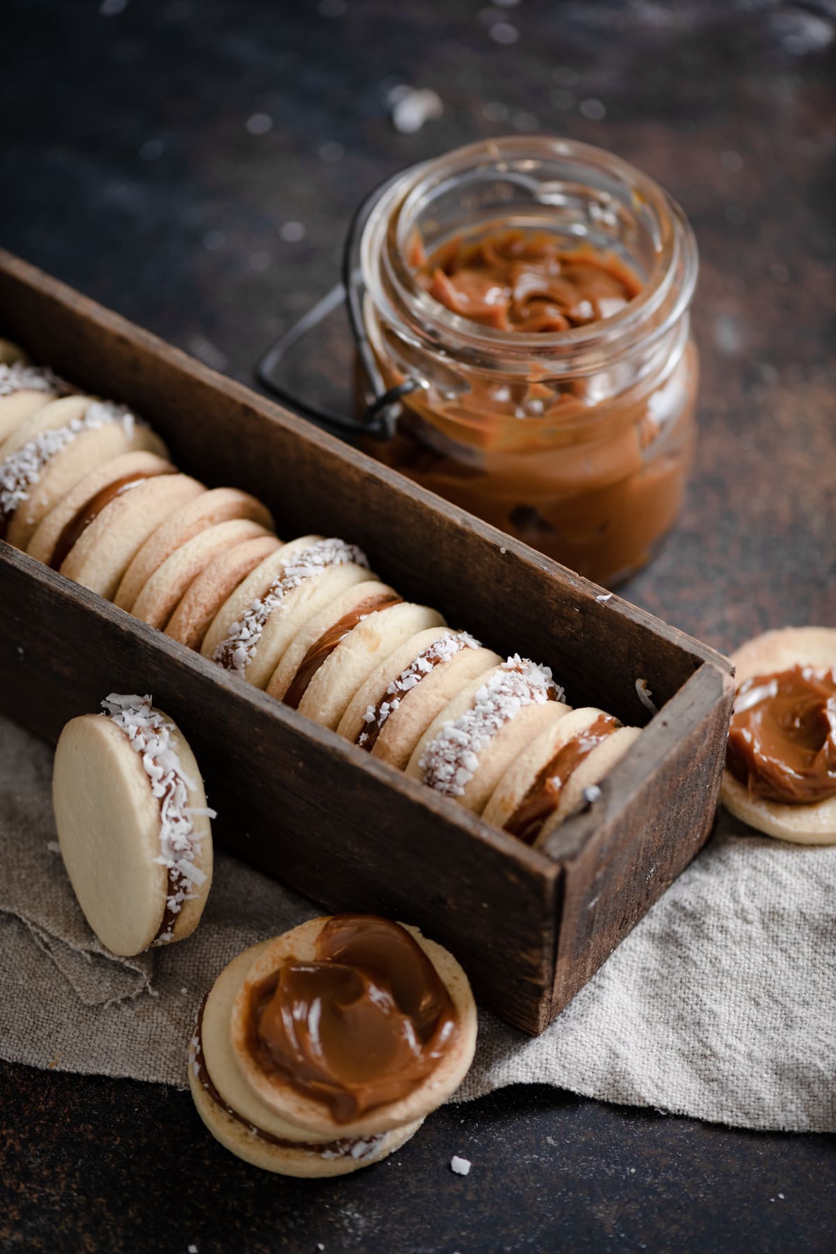 Alfajores Cookies in a box set on a cloth with dulce de leche in the background.
