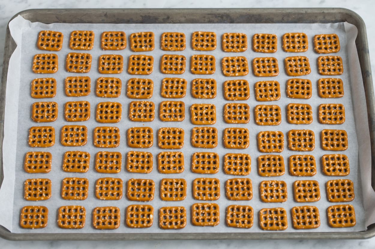 Pretzel M&M Hugs Showing how to make easy christmas treat. Putting square pretzels lined up in rows on a parchment paper lined baking sheet.