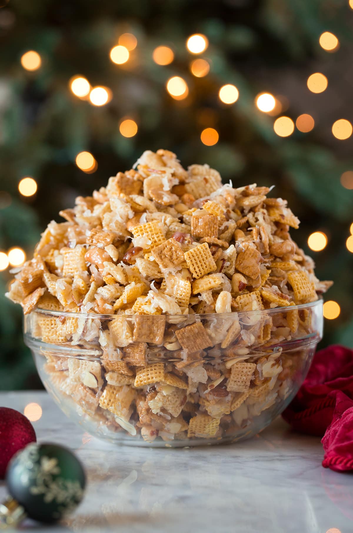 Sweet Chex Mix in front of a Christmas tree in a glass bowl.