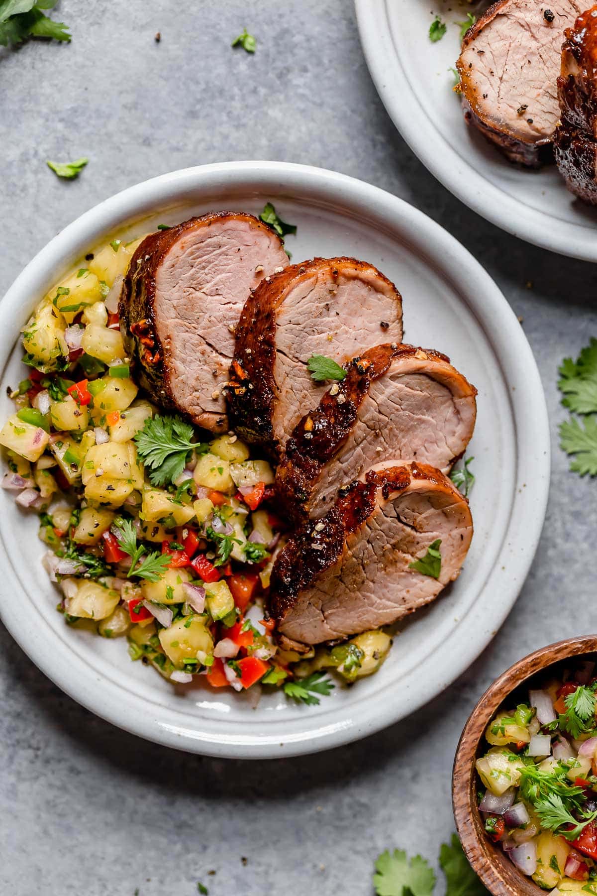 Pork tenderloin cut into slices on a serving plate with a side of pineapple salsa.