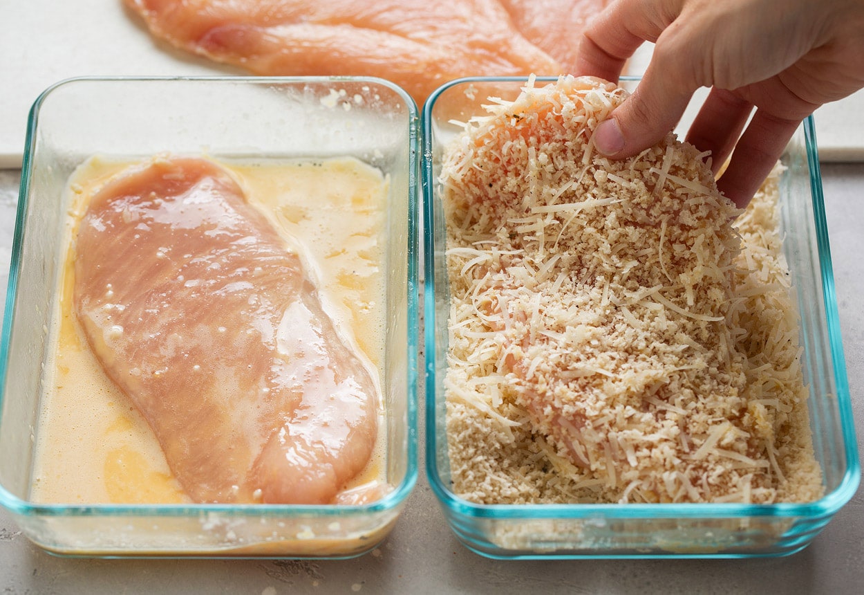 Showing how to make chicken parmesan. Dredging chicken cutlets in egg in shallow glass dish on left side then Panko parmesan mixture in shallow glass dish on right side.