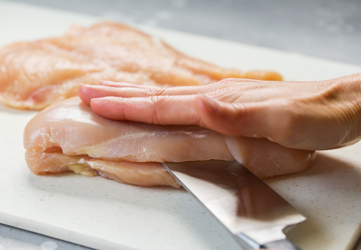 Showing how to make chicken parmesan. Starting by butterflying chicken breasts on a cutting board.