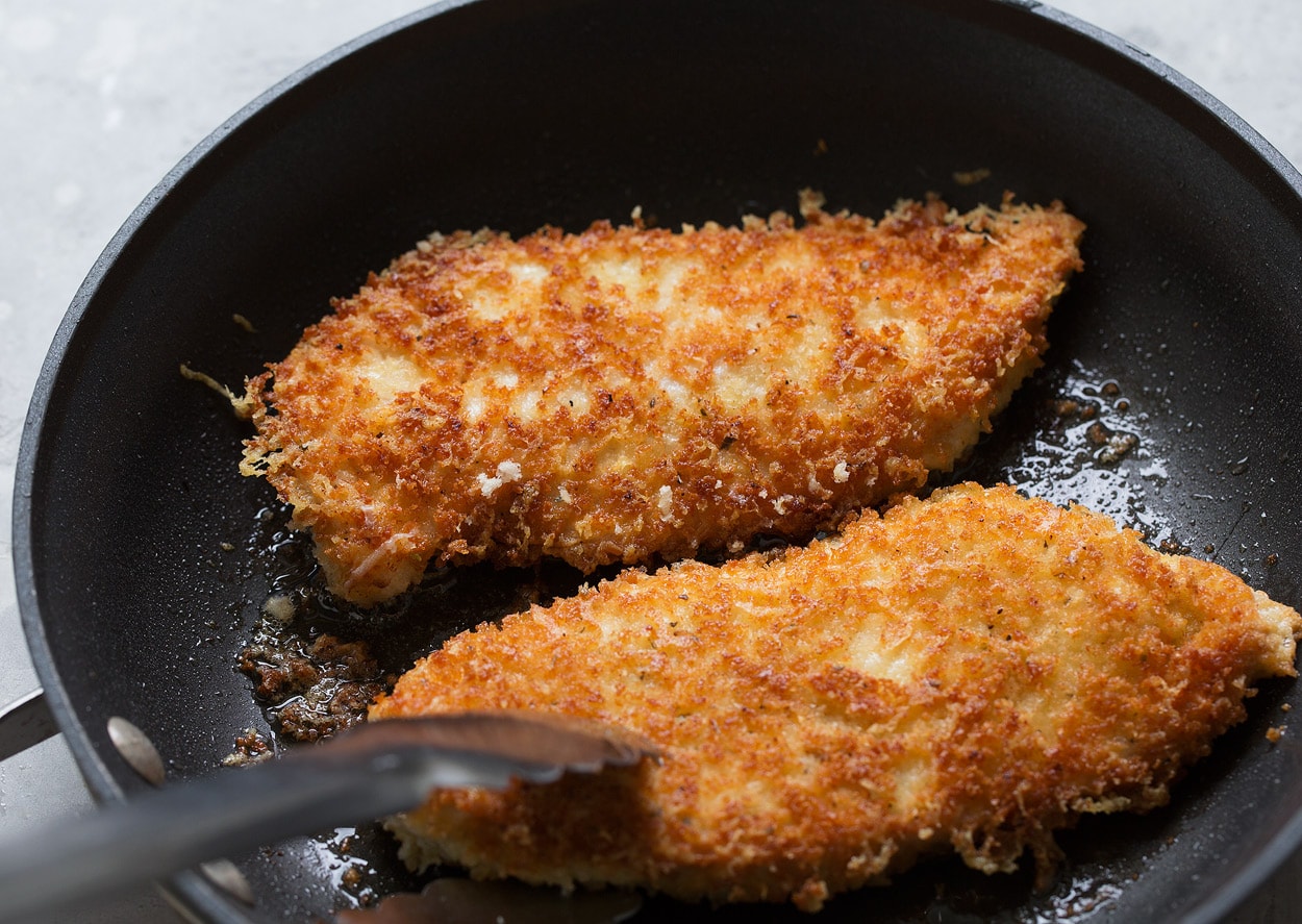 Searing chicken parmesan pieces in olive oil in black non-stick skillet until golden brown.
