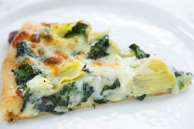 cheesy Artichoke pizza slice on white plate