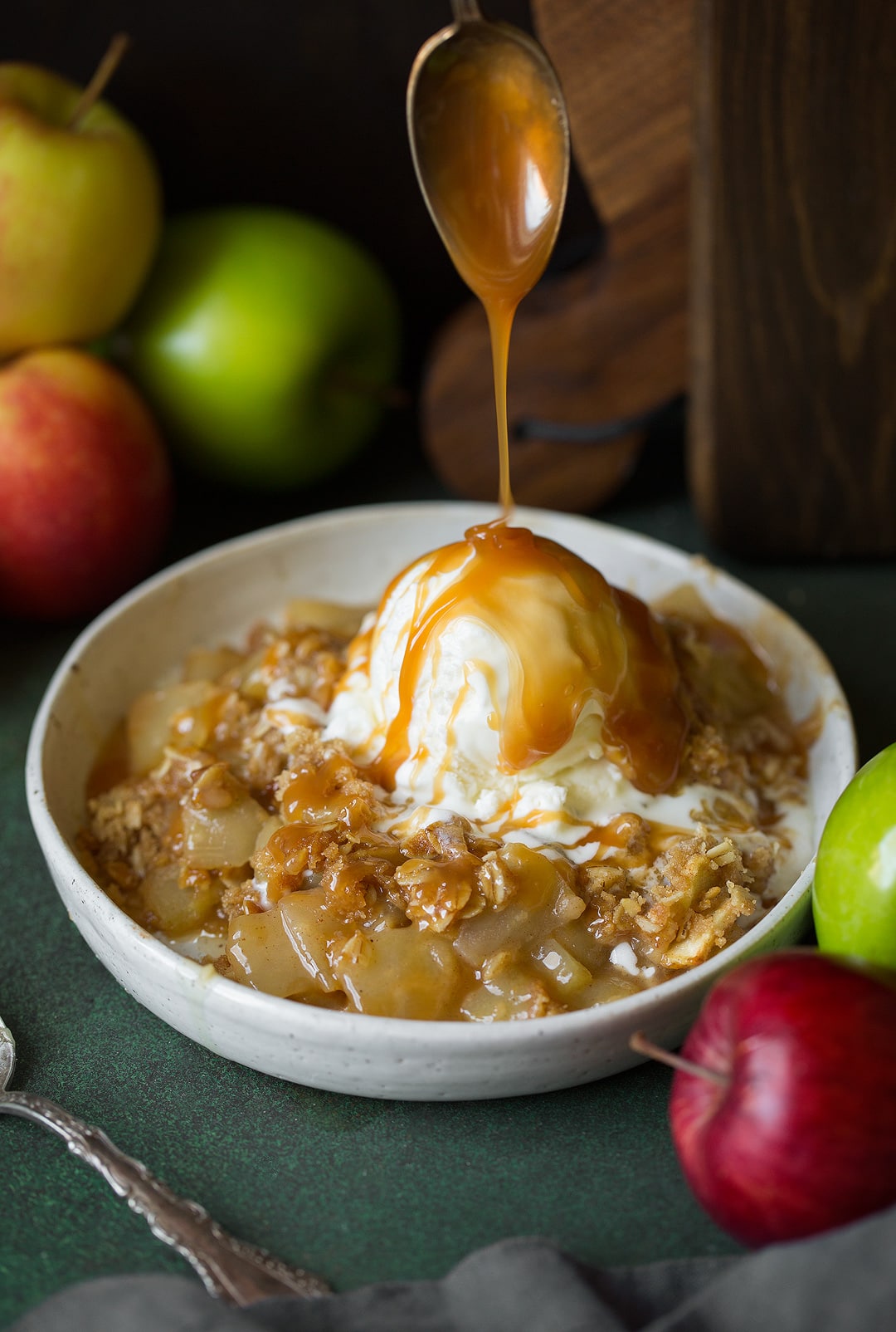 Drizzling caramel sauce onto a bowl of apple crisp and scoop of ice cream