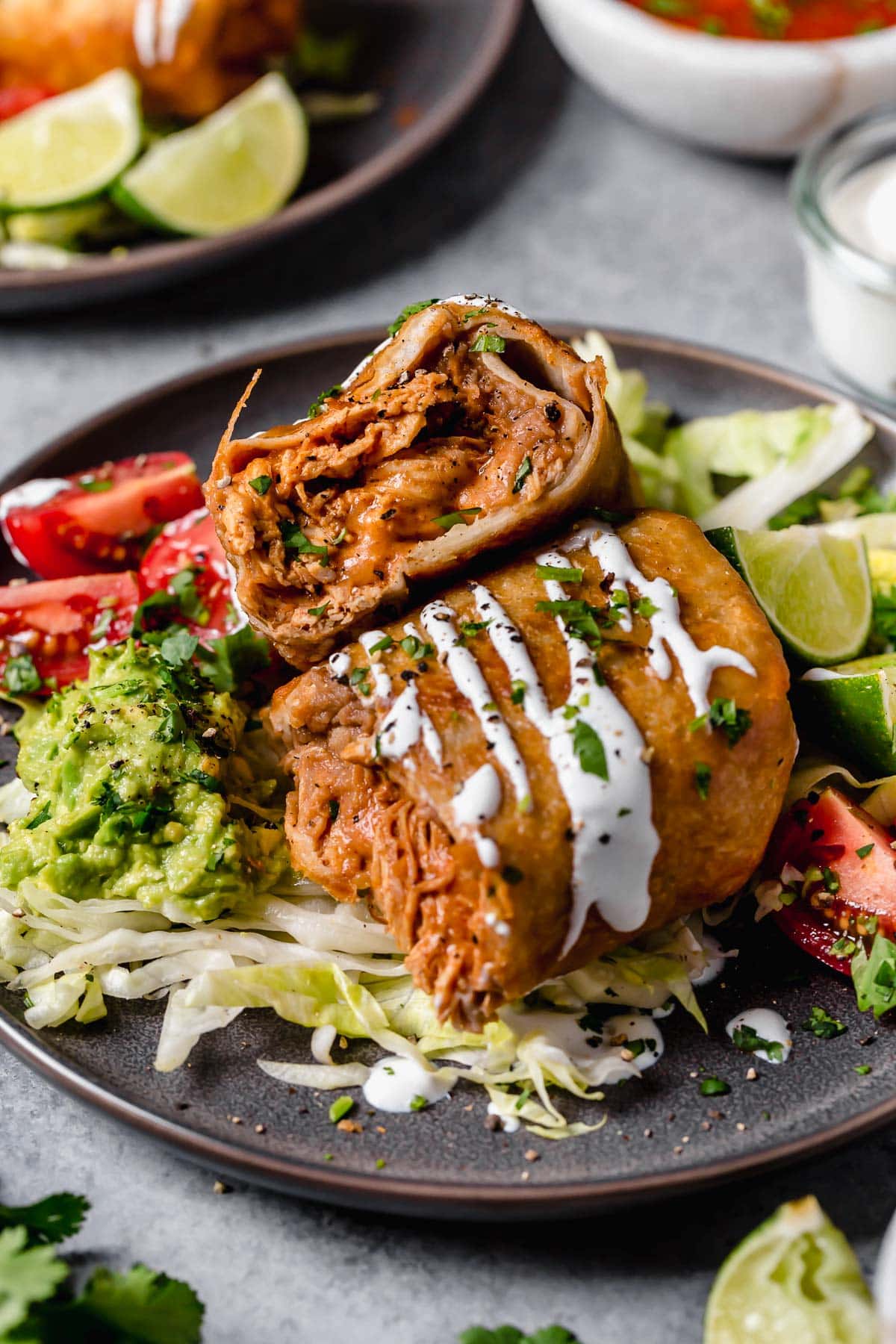 Chicken Chimichangas - one of the ultimate comfort foods! Perfectly hearty and layered with delicious ingredients like seasoned chicken, rich refried beans and shredded Mexican cheese. They're perfectly crisp and oh so satisfying! #chimichanga #chicken #mexican #recipe #refriedbeans #dinnerideas Homemade Chicken Chimichanga cut in half stacked. Filled with refried beans, and seasoned shredded chicken.