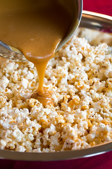Pouring caramel coating over plain popcorn in a large mixing bowl.
