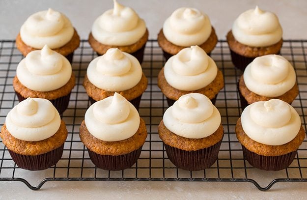 Adding cream cheese frosting to carrot cake cupcakes.