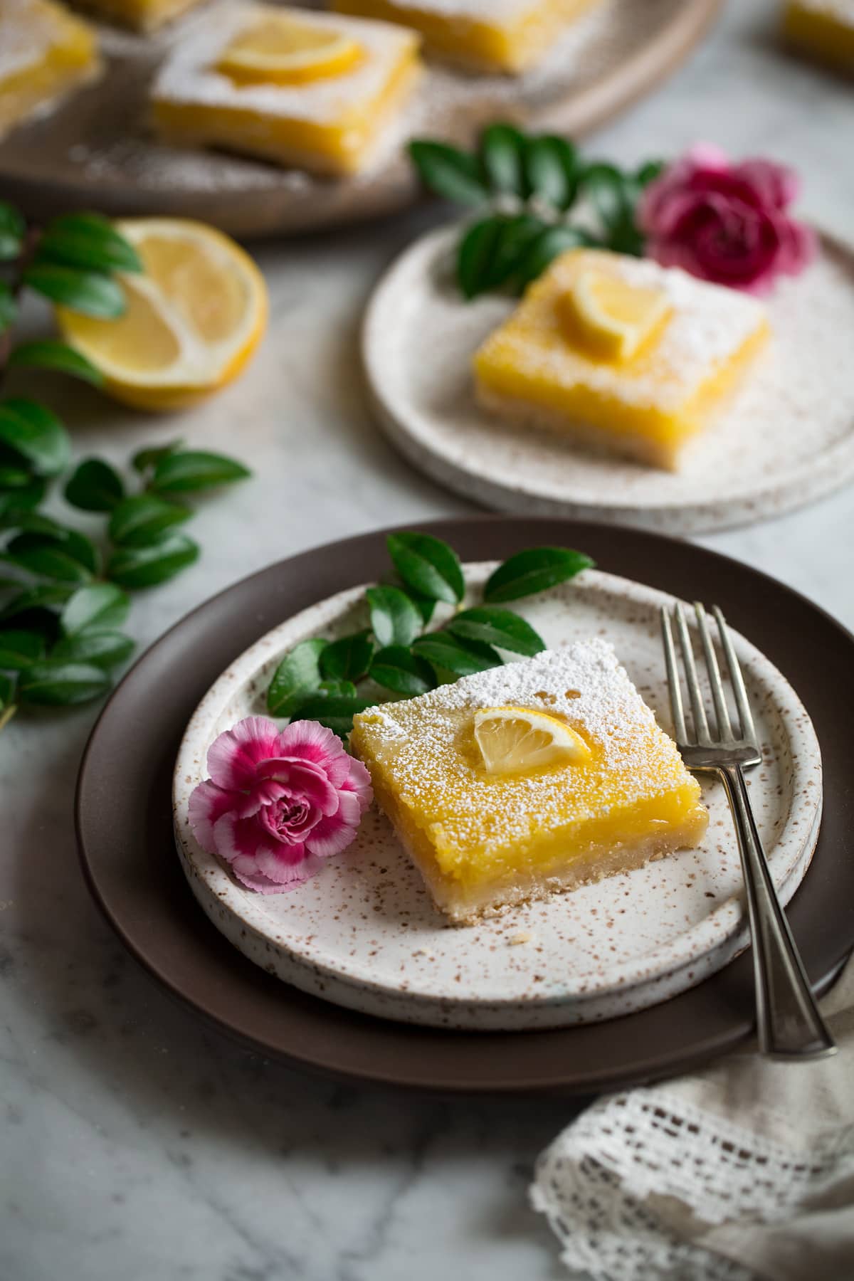 Lemon Bars or two dessert plates decorated with flowers and greens.
