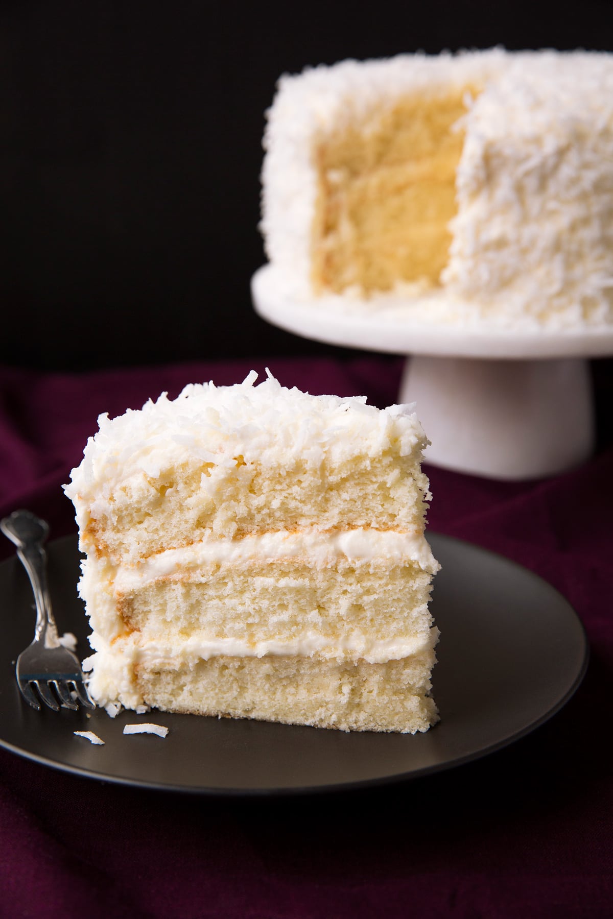 Single slice of easy coconut cake with a remainder of cake in the background.