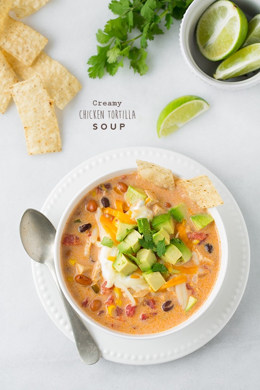 Creamy Chicken Tortilla Soup. A hearty, warming and comforting soup made with juicy chicken, vegetables and loaded with delicious toppings. Best of all this soup is whipped up in under 30 minutes and couldn't be easier! | Chicken Soup | Mexican Soup | #veggiesdontbite #soup #chicken #tortilla An overhead shot of Creamy Chicken Tortilla Soup in a bowl topped with avocado and lime wedges at the side