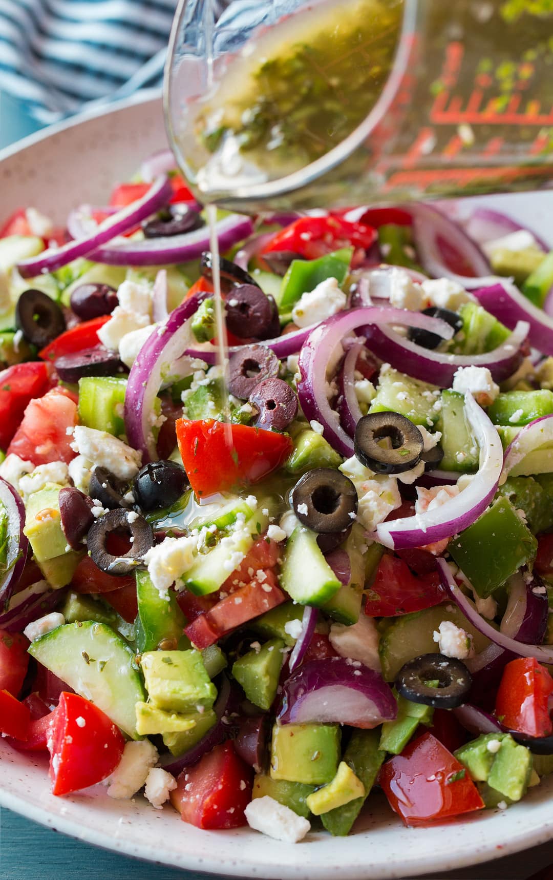 Greek Salad in a bowl with dressing getting poured over