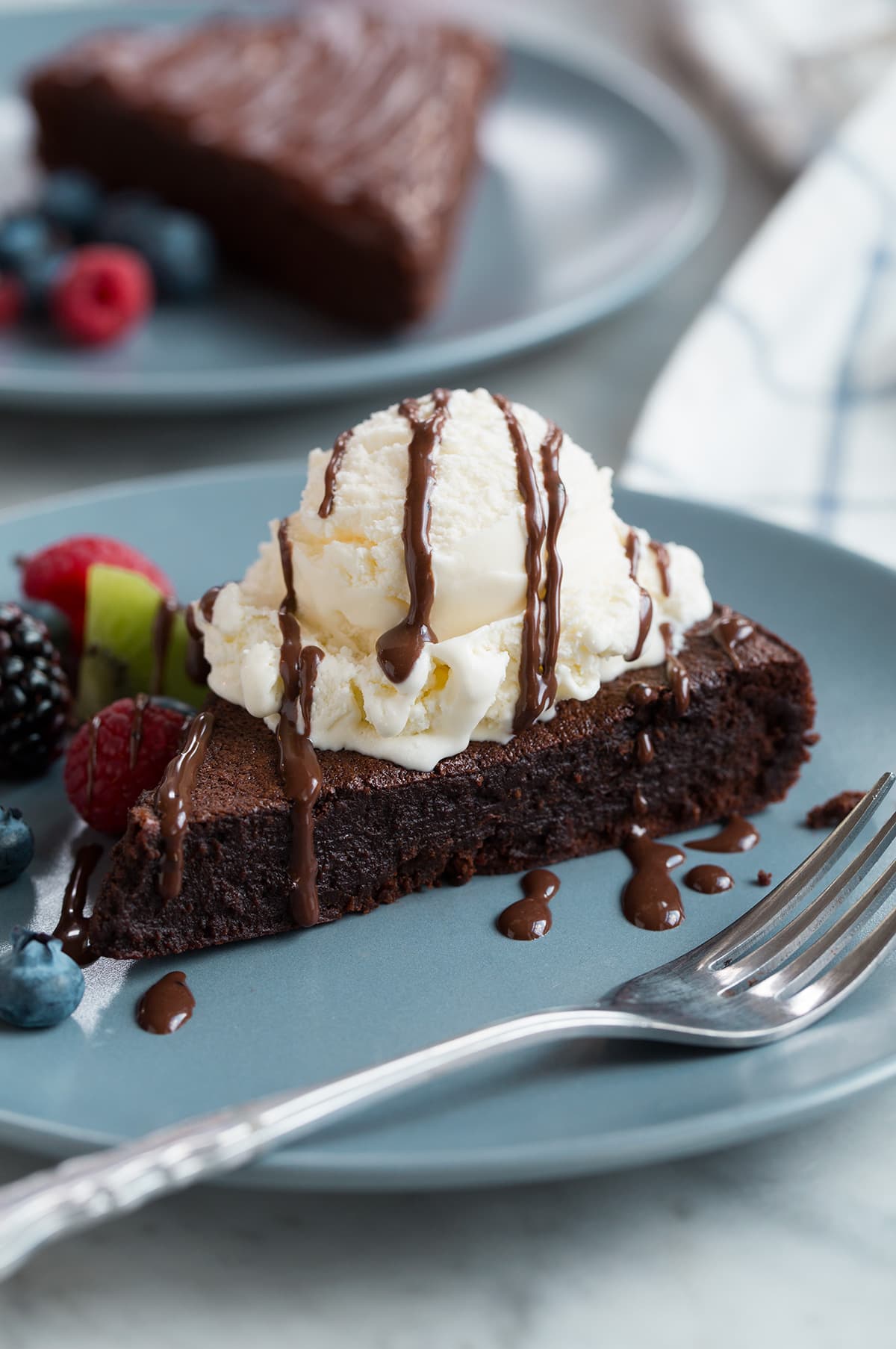 Flourless Chocolate Cake on a blue serving plate. Cake is topped with vanilla ice cream and fudge sauce.