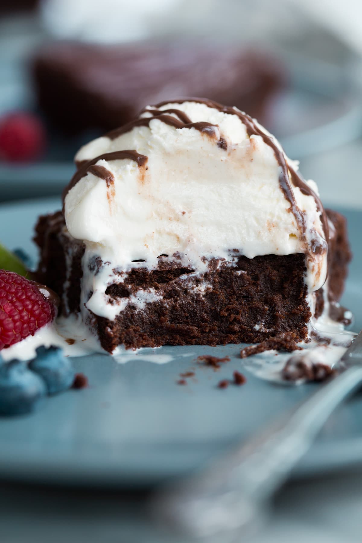 Flourless chocolate cake with several bites eaten to showing. It's topped ice cream and chocolate sauce. 