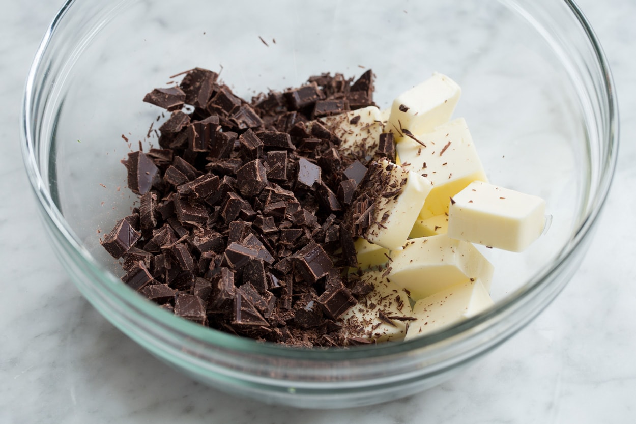 Showing how to make flourless chocolate cake, adding chopped chocolate and butter to a glass mixing bowl.