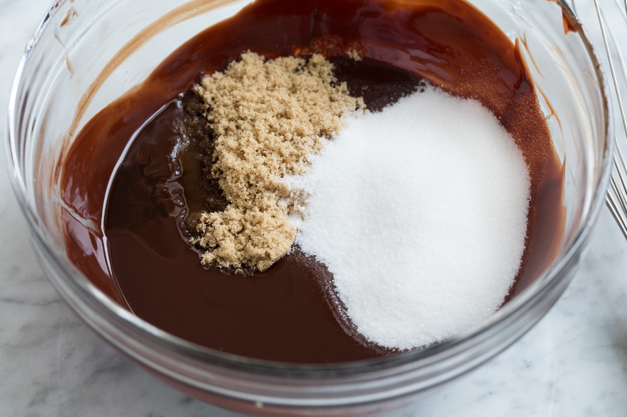 Mixing sugars into melted chocolate mixture in mixing bowl.