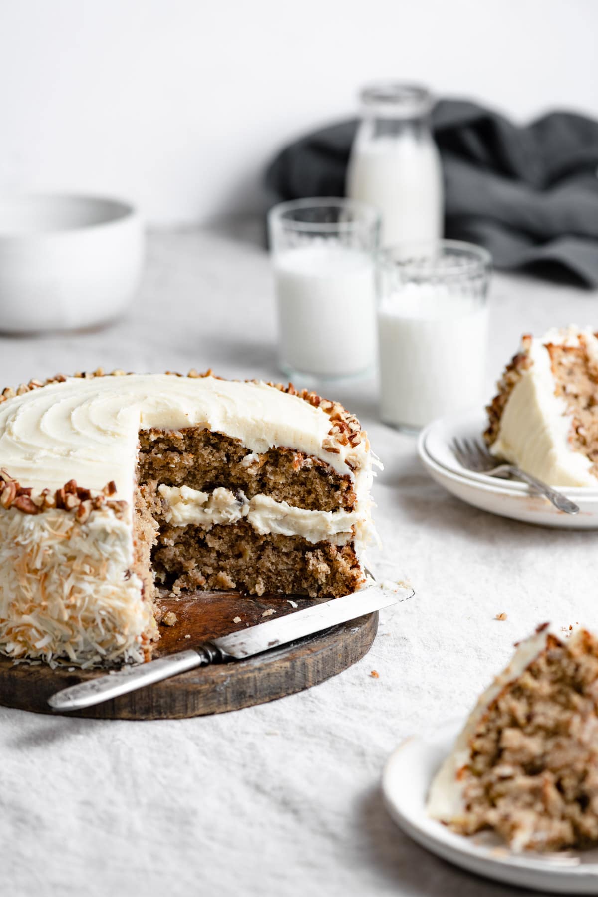 Hummingbird cake shown with a quarter of the cake removed, cake is sitting on a wooden platter. Slices of cake are shown of the the right side.