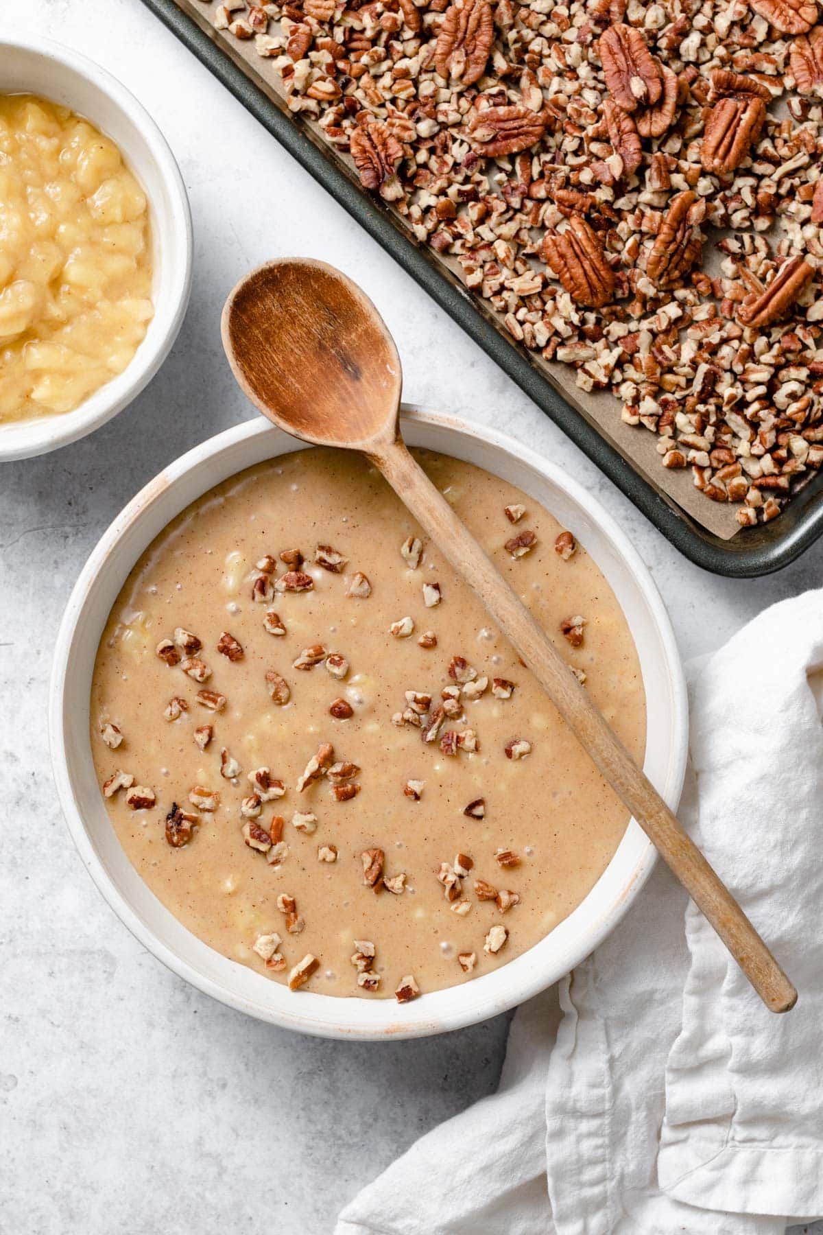 Showing how to mix cake batter ingredients in a ceramic mixing bowl using a wooden spoon to fold in pecans.
