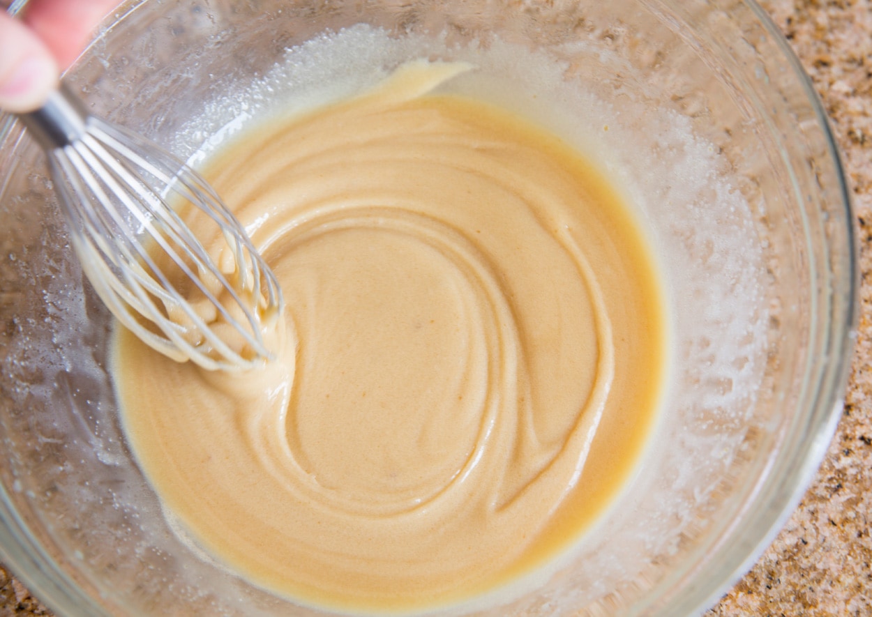 Showing how to make caramel. Whisking butter, corn syrup, sweetened condensed milk, salt and sugar in glass mixing bowl.