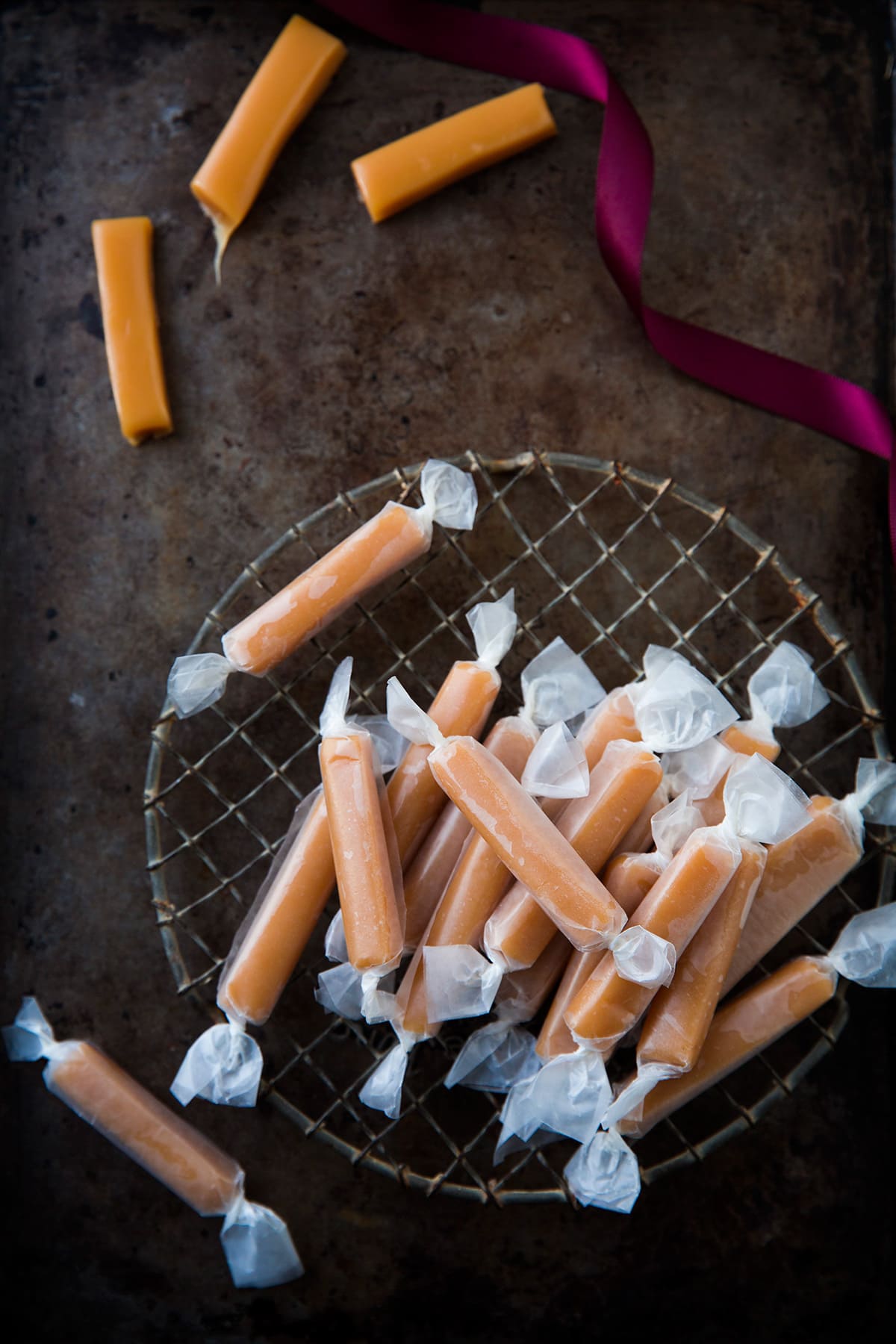 Stack of caramels wrapped in wax paper with several cut caramels unwrapped off to the side.