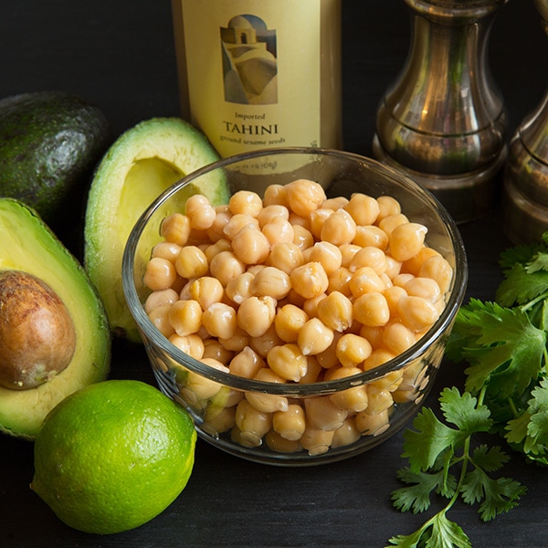 This creamy delicious homemade hummus recipe is the best! It can be made in under 10 minutes and it makes the perfect midday snack for you and your family, or take it to a party and impress your friends! #cookingclassy #hummus #avocado #dips A bowl of chickpeas with other ingredients to make avocado hummus at the side