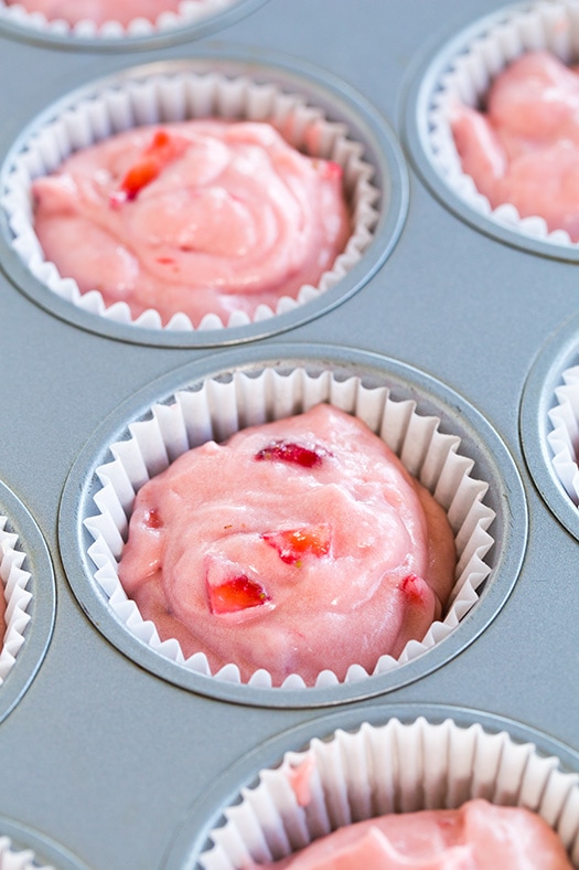These Strawberry Cupcakes are made with chunks of fresh strawberries in the cake batter and are topped with a luscious pink Strawberry Buttercream Frosting. Bursting with flavor, these cupcakes would go down a treat at any celebration! #cookingclassy #cupcakes #strawberry #buttercream #cakes A process shot of filling cupcake cases with strawberry cupcake batter