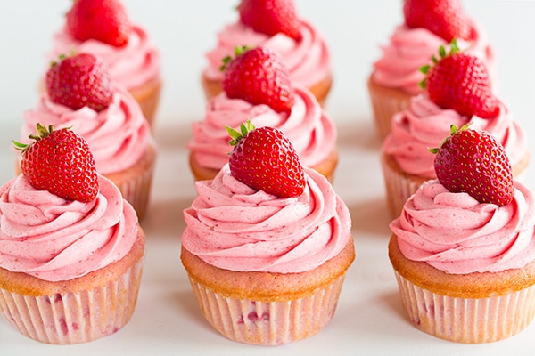 These Strawberry Cupcakes are made with chunks of fresh strawberries in the cake batter and are topped with a luscious pink Strawberry Buttercream Frosting. Bursting with flavor, these cupcakes would go down a treat at any celebration! #cookingclassy #cupcakes #strawberry #buttercream #cakes Three rows of strawberry cupcakes topped with strawberry buttercream and fresh strawberries