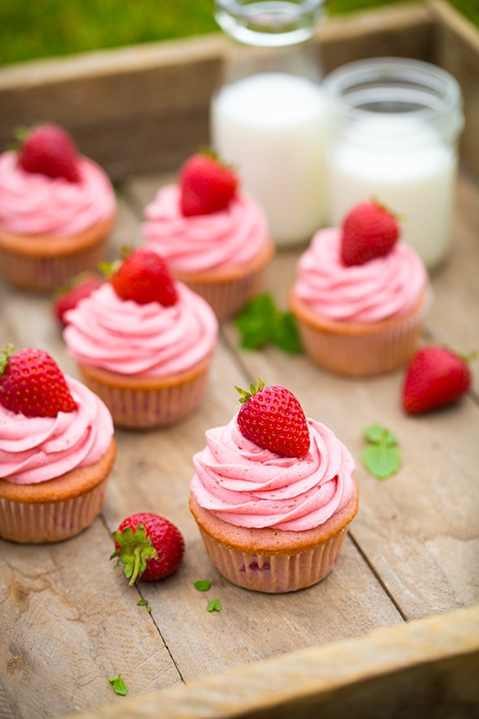 These Strawberry Cupcakes are made with chunks of fresh strawberries in the cake batter and are topped with a luscious pink Strawberry Buttercream Frosting. Bursting with flavor, these cupcakes would go down a treat at any celebration! #cookingclassy #cupcakes #strawberry #buttercream #cakes Strawberry cupcakes on a wooden tray
