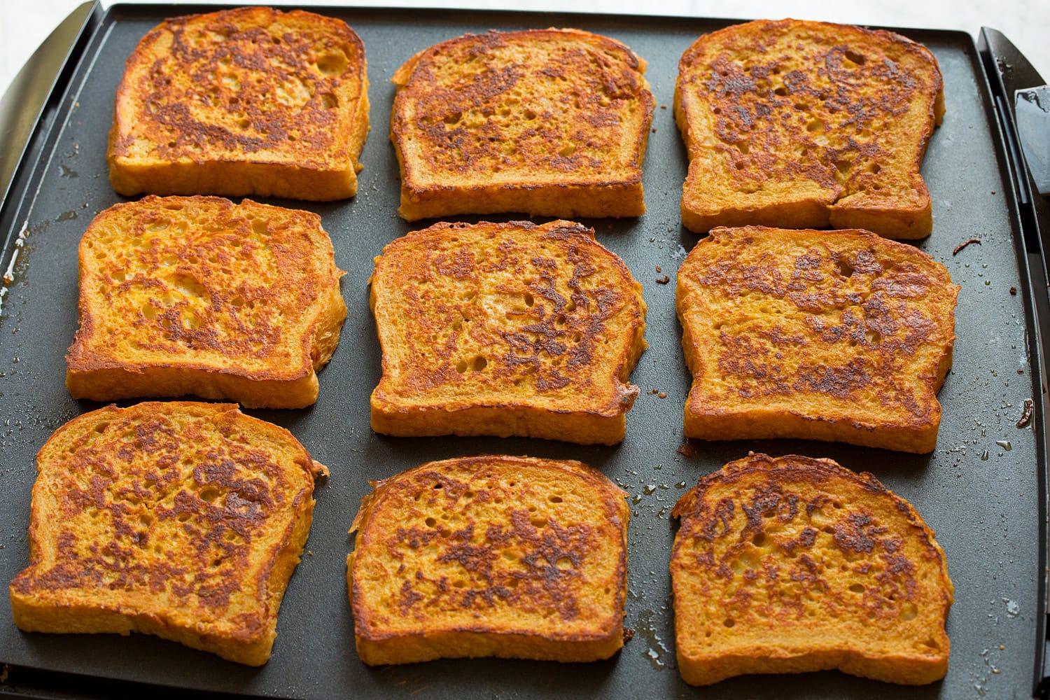Pumpkin french toast cooking on a large non-stick griddle.