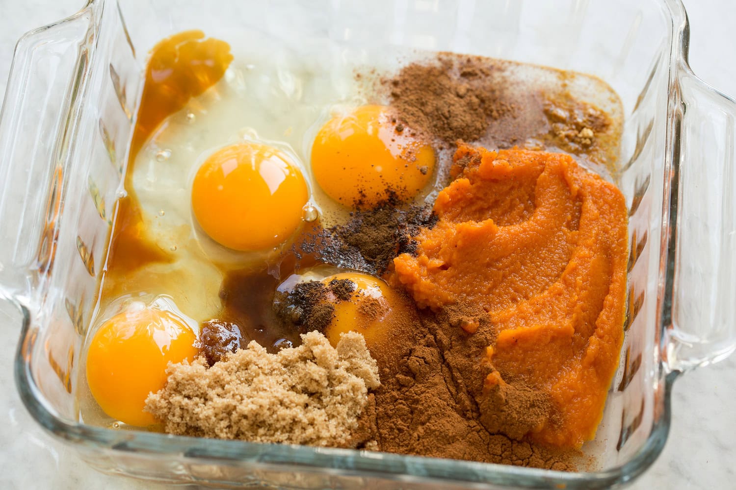Pumpkin, eggs, spices, sugar in a glass dish shown before mixing.