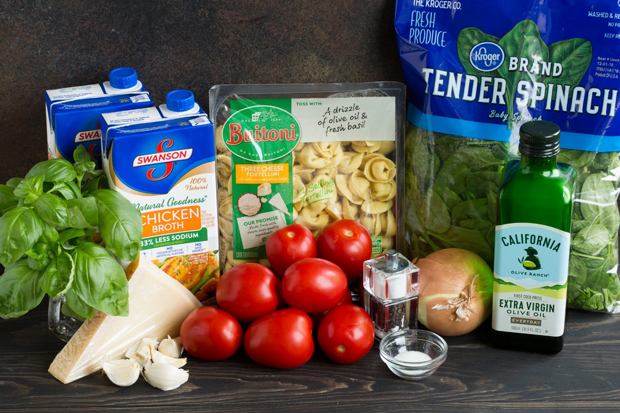 Ingredients needed to make tortellini soup shown here including tortellini, spinach, tomatoes, onion, parmesan, garlic, chicken broth, basil, olive oil.