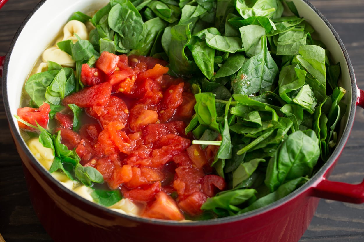 Adding fresh tomato and spinach to tortellini soup.