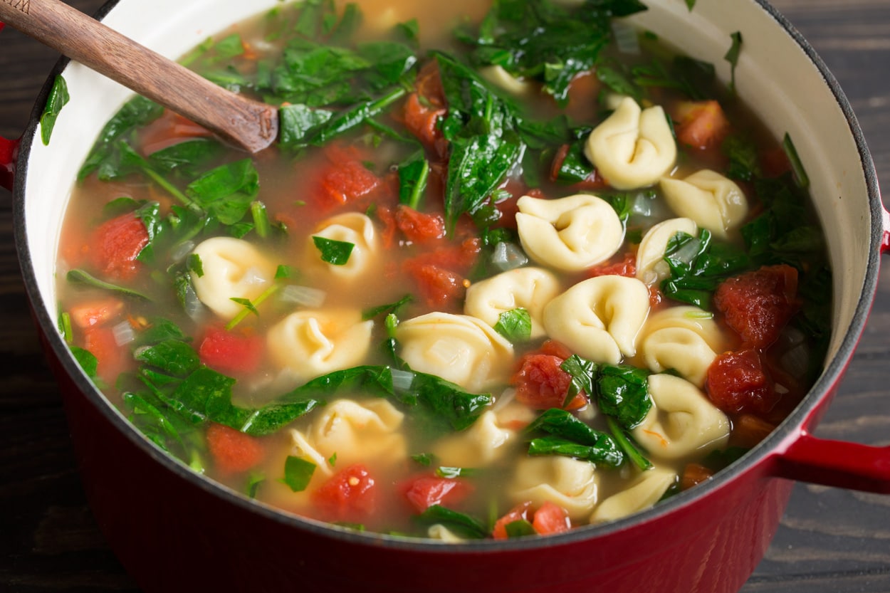 Completed tortellini soup in a large red cast iron pot with a wooden spoon.