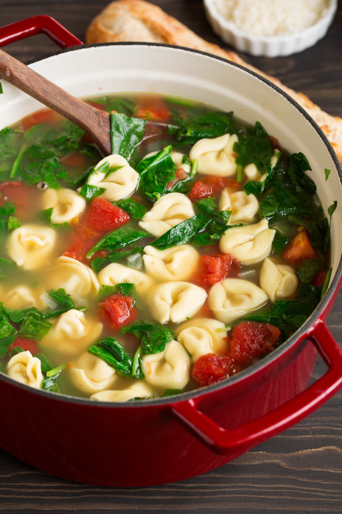 Close up image of tortellini soup in a red pot set over a wooden tabletop.