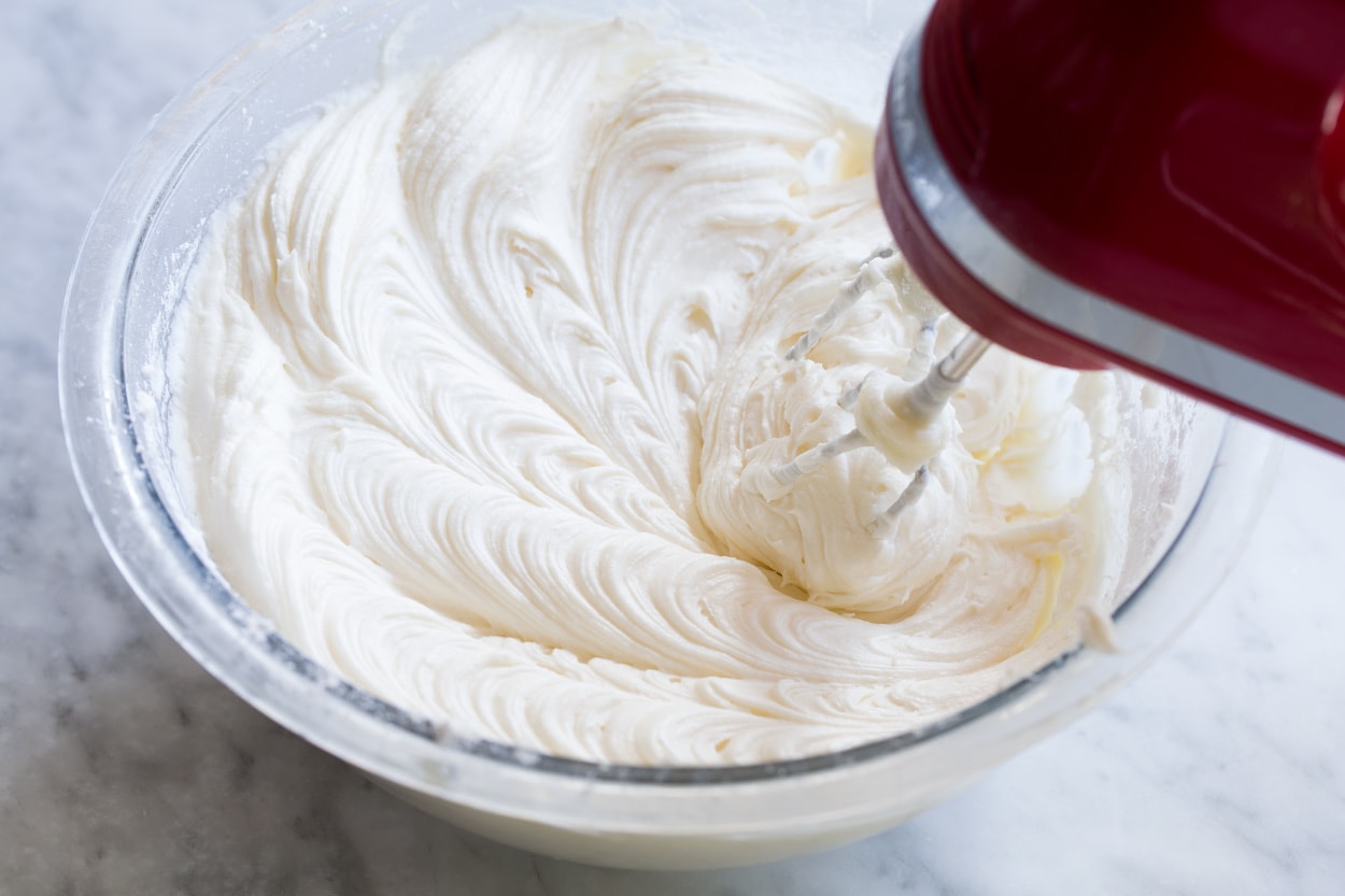 Mixing cream cheese frosting in glass mixing bowl with an electric hand mixer.