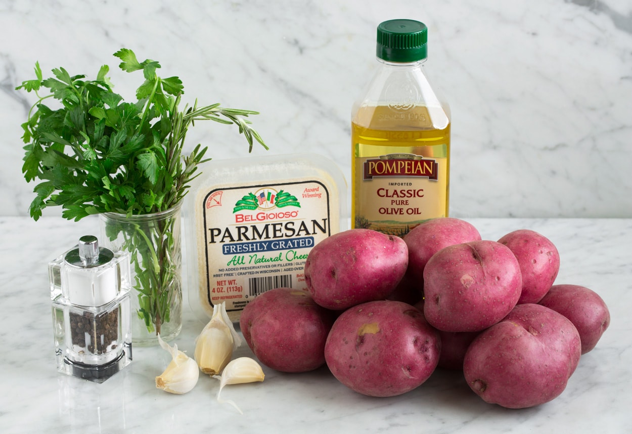 Ingredients needed for herb roasted potatoes shown here including red potatoes, olive oil, parmesan, garlic, herbs, salt and pepper.
