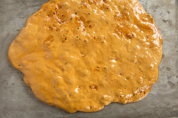 Spreading finished peanut brittle mixture onto baking sheet.