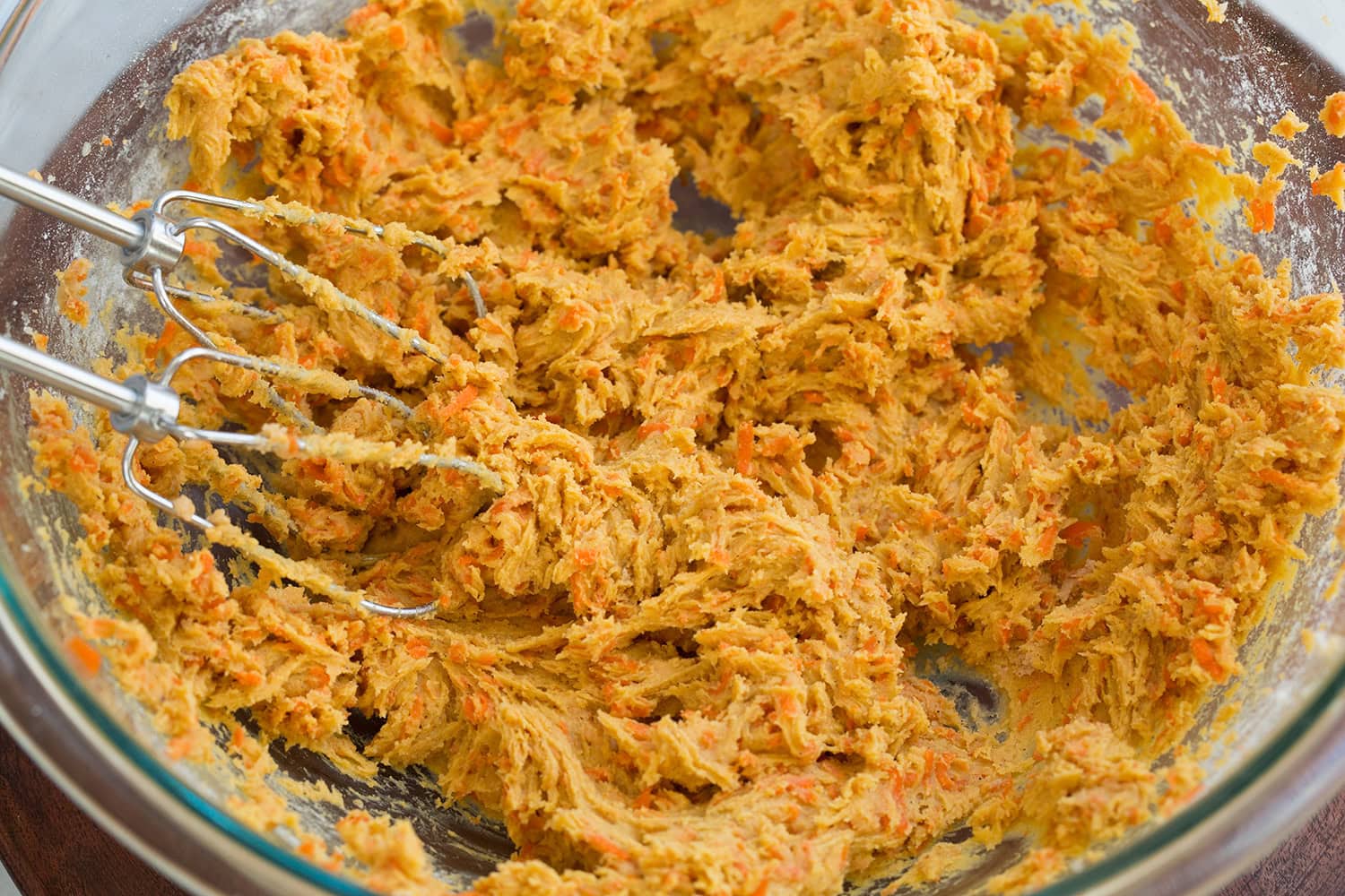 Completed carrot cookie dough batter in glass mixing bowl.