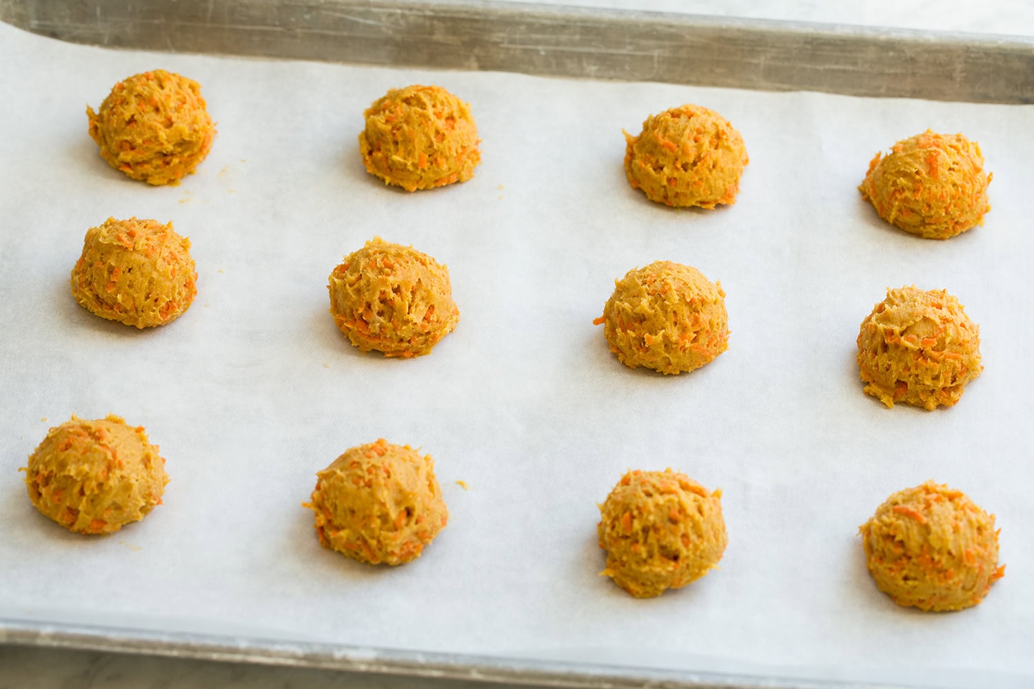 Carrot cookie dough rounds on baking sheet shown raw before baking.