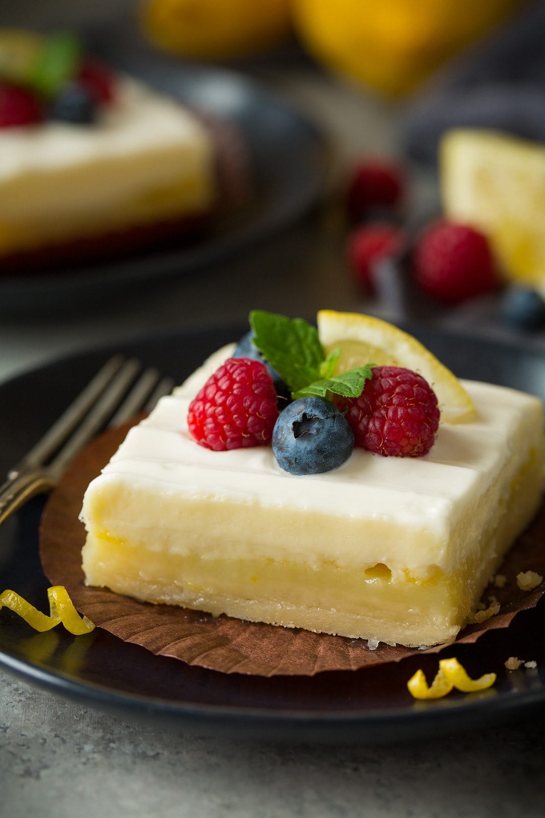 close up of Lemon Cheesecake Bar garnished with berries, lemon, and fresh mint