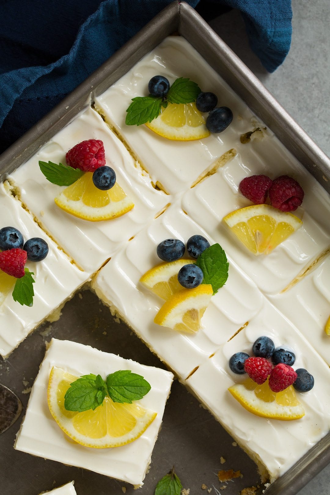 pan of Lemon Cheesecake Bars, sliced and garnished with berries and lemon wedges
