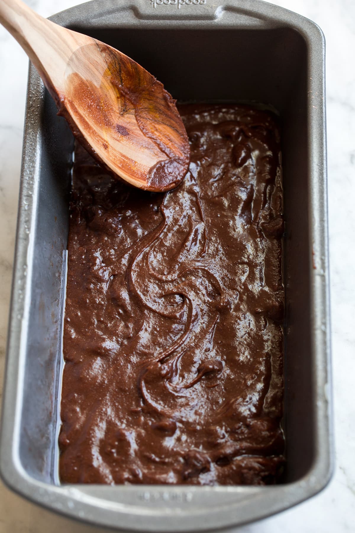Brownie batter being spread into a bread pan.