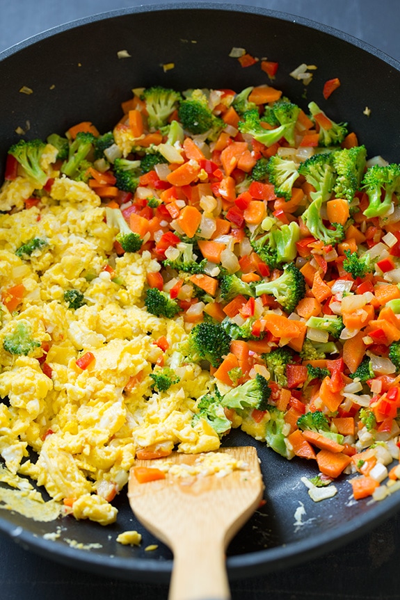 vegetables and cooked eggs in a skillet with a wooden spoon